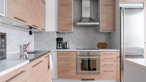 Una cocina moderna con armarios de madera clara, un refrigerador de acero inoxidable, horno empotrado y cafetera.
