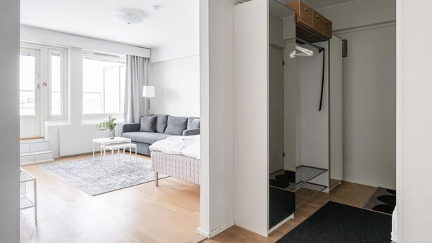 Una habitación moderna y luminosa con un sofá gris, una mesita blanca pequeña y una alfombra gris.
