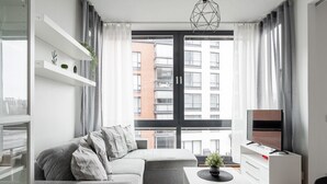 A modern living room with a grey sofa, a coffee table, a TV on a stand, and a large window with curtains.