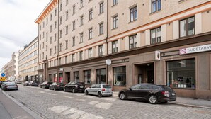 Un immeuble à plusieurs étages, avec une rangée de voitures garées le long de la rue.