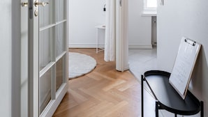 Un couloir avec un plancher en bois, une porte blanche dotée de panneaux de verre et une table noire sur laquelle se trouve un presse-papiers.