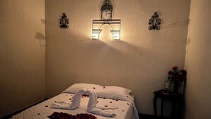 A hotel room with a bed, a wall-mounted light fixture, and a small table with a bottle and flowers. - Jireh Antigua (Antigua Guatemala)