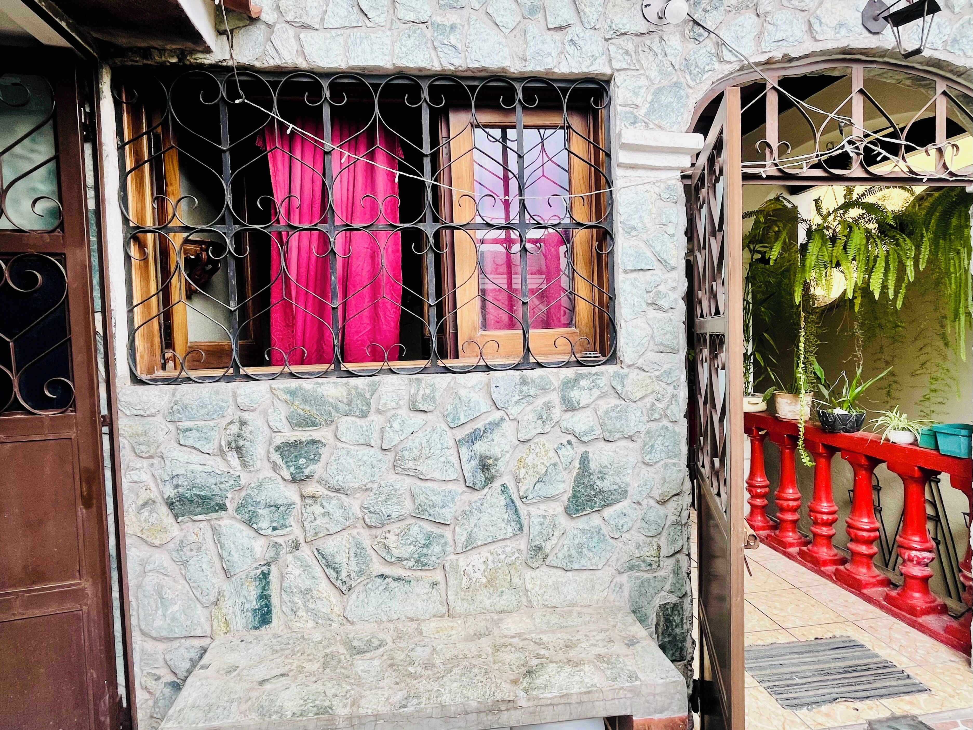 Un edificio de piedra con una ventana que tiene barrotes de metal y cortinas rojas.