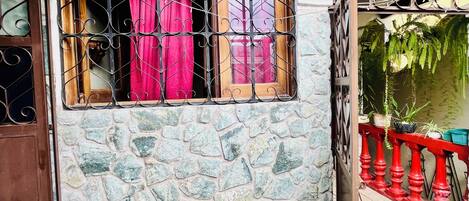 Un edificio de piedra con una ventana que tiene barrotes de metal y cortinas rojas.