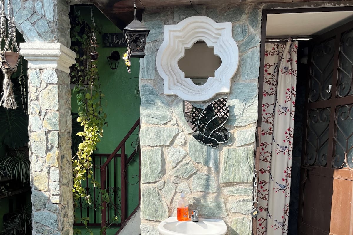 A stone-walled outdoor area with a white pedestal sink, a decorative wall piece, and a potted plant.