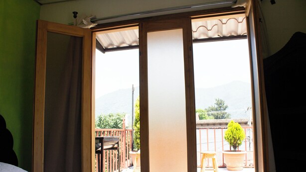 A room with a bed, a sliding door leading to an outdoor balcony with a view of mountains and a potted plant. - Jireh Antigua (Antigua Guatemala)