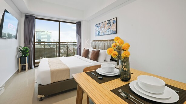 Une chambre d’hôtel moderne avec un grand lit, une table à manger avec de l’assiette blanche et un vase de fleurs, et une vue sur la ville par la fenêtre.