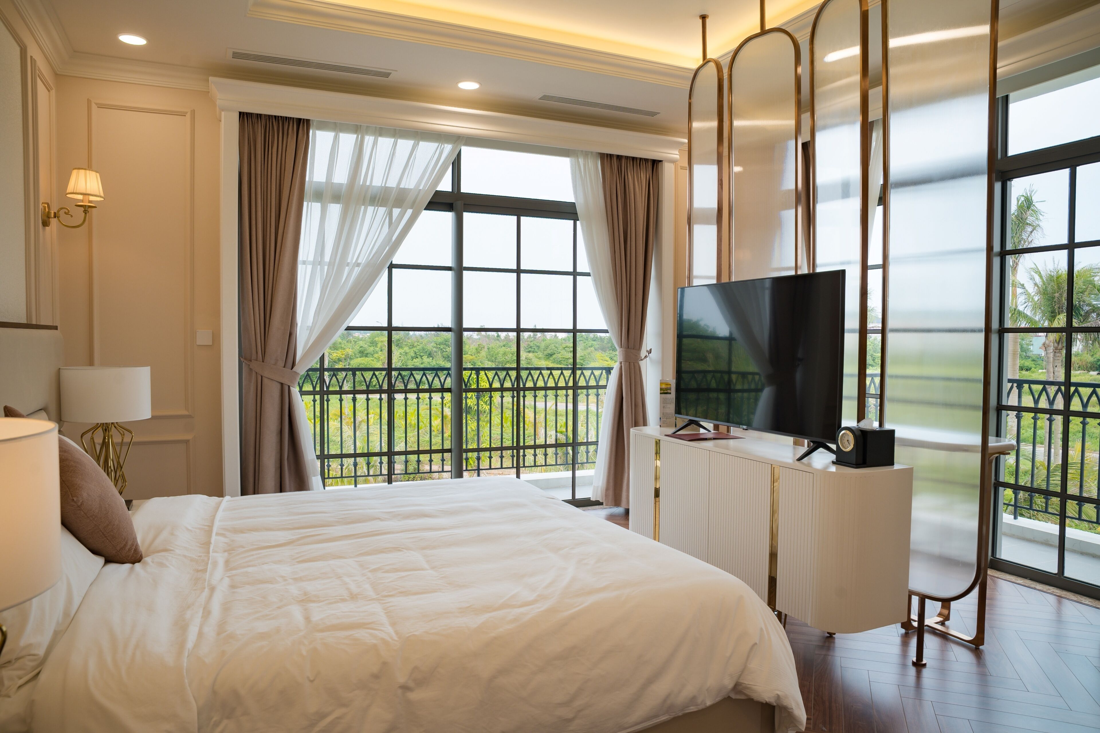 Habitación de hotel con una cama grande, televisión y balcón con vistas a zonas verdes.