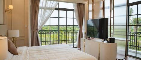 Habitación de hotel con una cama grande, televisión y balcón con vistas a zonas verdes.