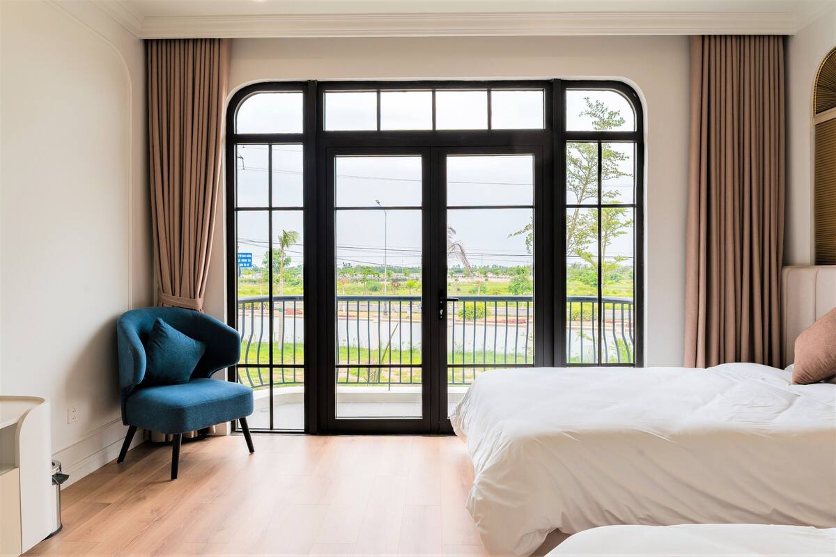 A bedroom with a large window, a bed, a chair, and a view of a green landscape.