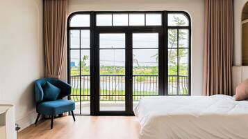 A bedroom with a large window, a bed, a chair, and a view of a green landscape.
