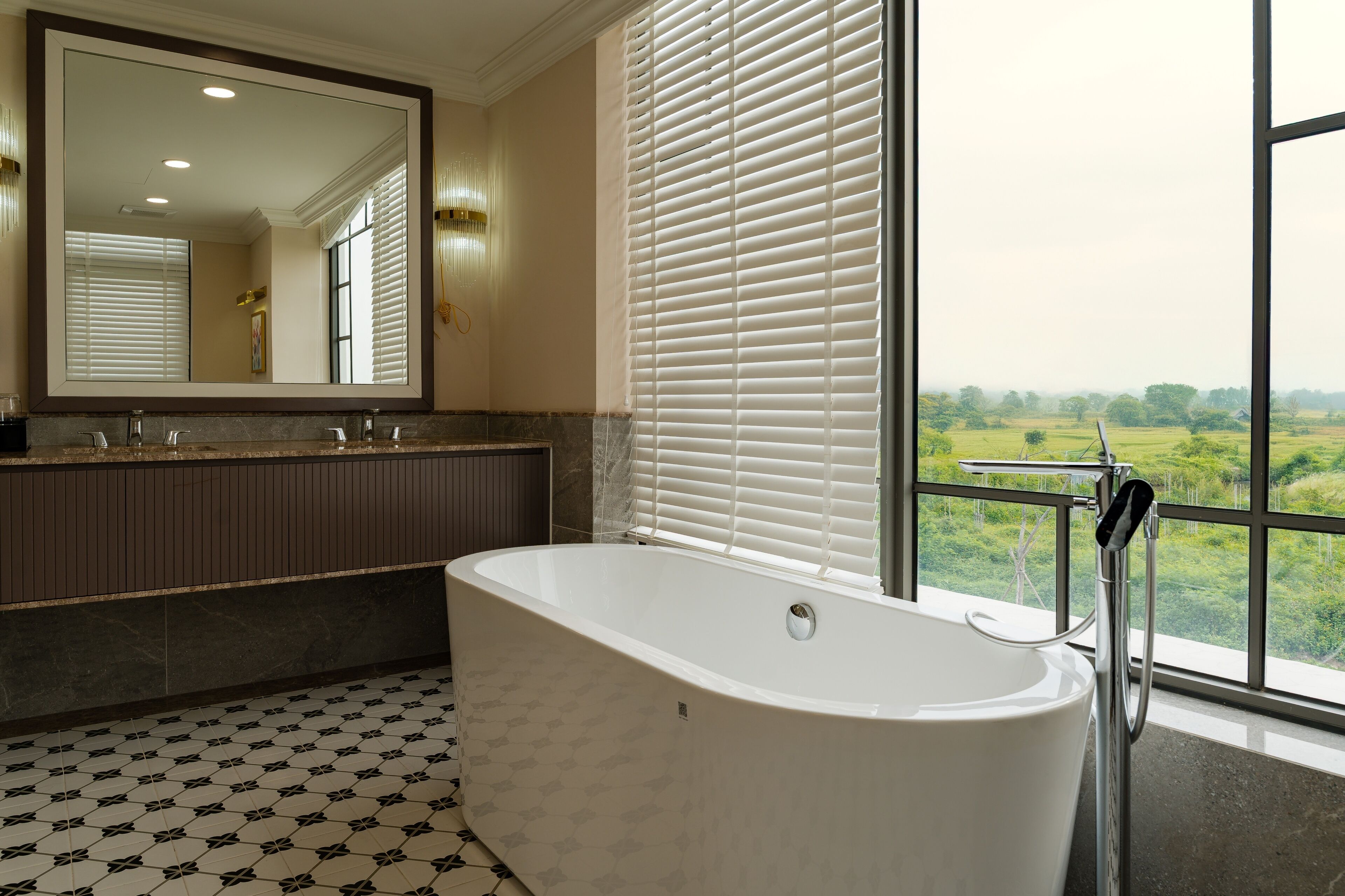Een moderne badkamer met een vrijstaand bad, een grote spiegel en uitzicht op een groen landschap door grote ramen.
