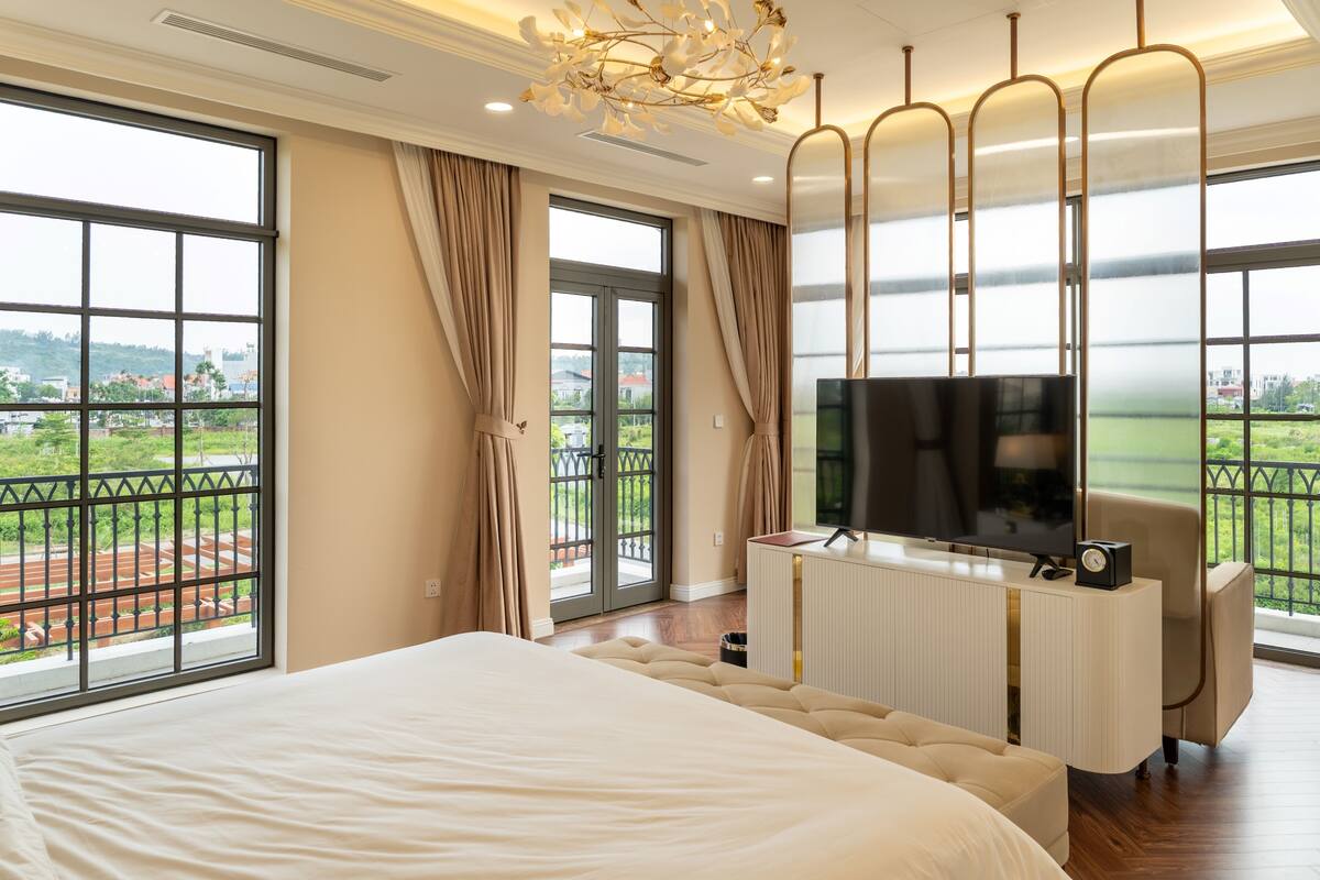 A hotel room with a large bed, a TV, a desk, and a view of the outdoors.