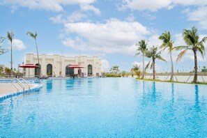 A swimming pool with a building in the background, palm trees, and a clear sky. - Ruby Tree Golf Villas (Hai Phong)