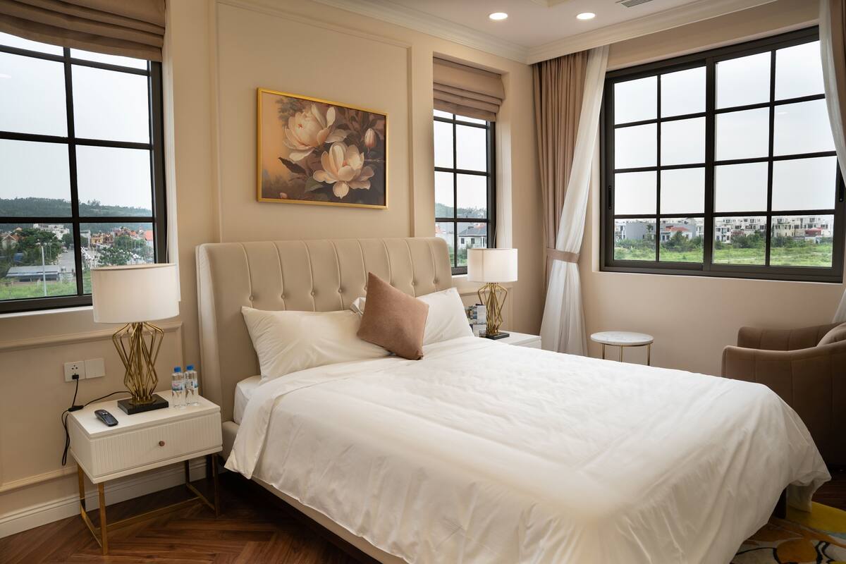 A hotel room with a large bed, a nightstand with a lamp, a chair, and a painting on the wall.