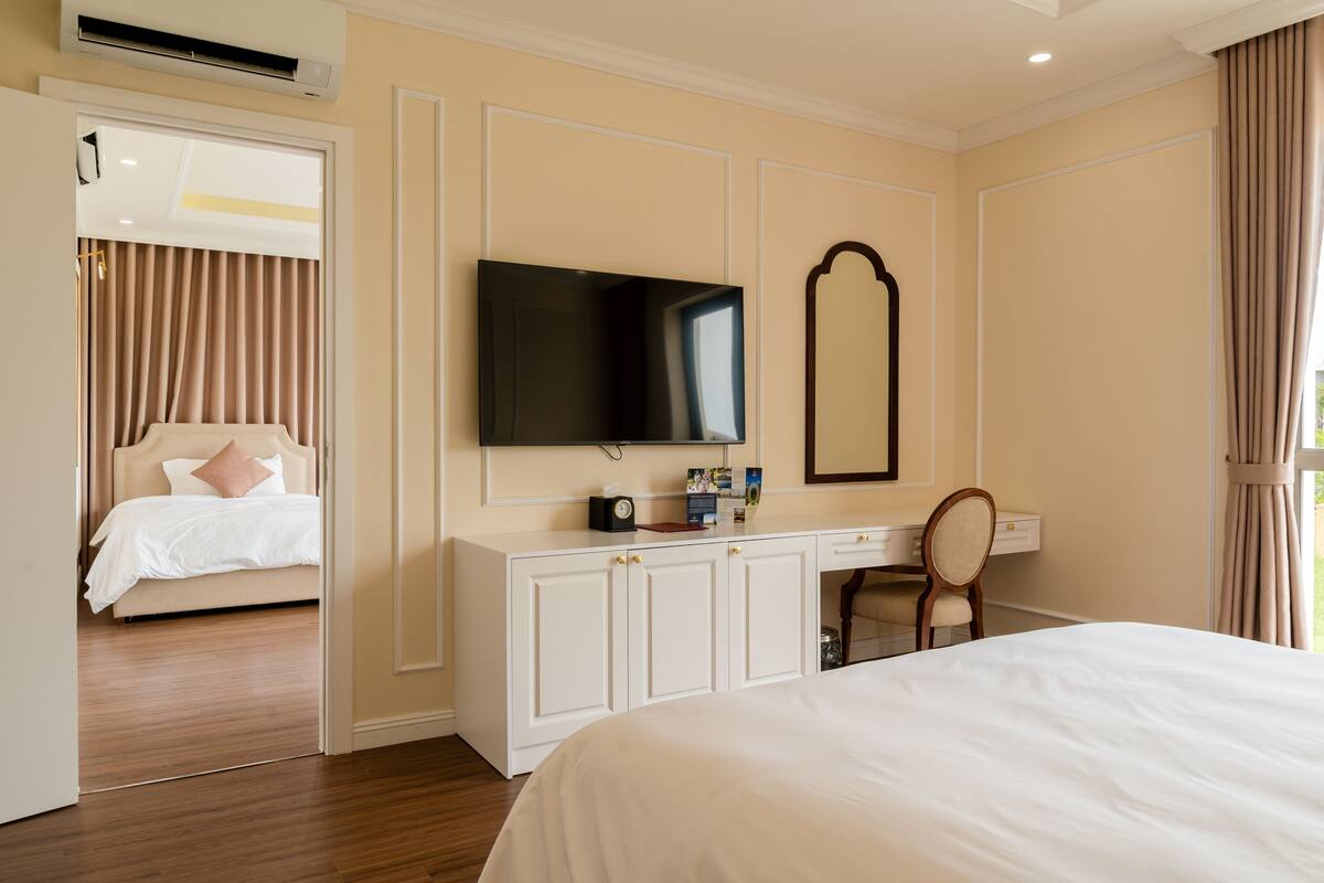 A hotel room with a bed, a desk with a flat-screen TV, a mirror, and a wardrobe.