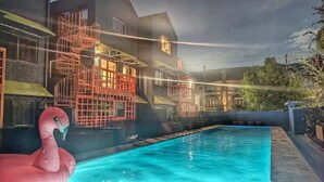 En swimmingpool med en lyserød flamingo-badeting, en trappe og en bygning med gelænder i rødt.