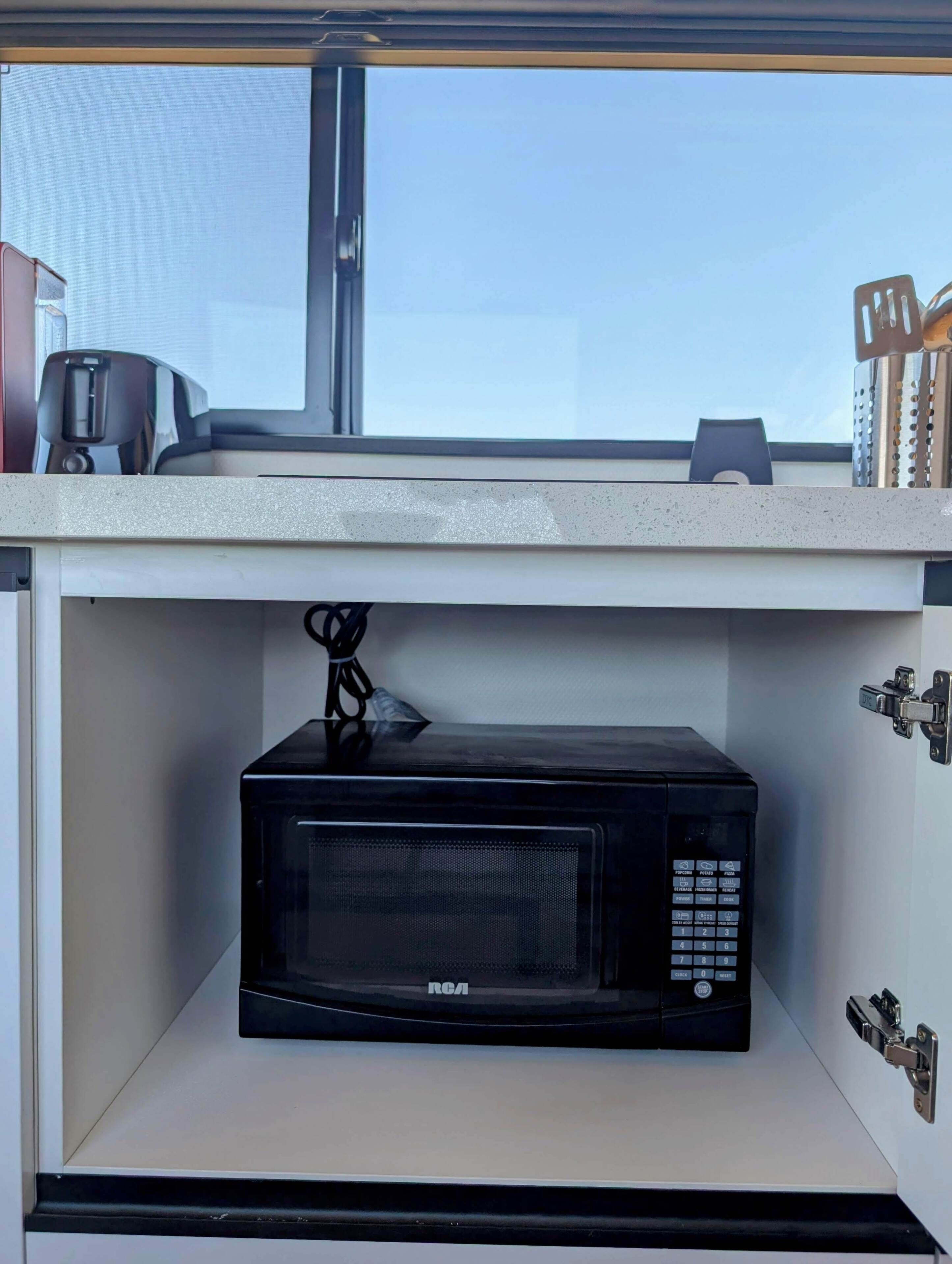 Una cucina con un forno a microonde RCA nero sotto una finestra.