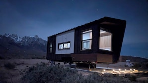 A modern, elevated house with large windows, situated in a desert with mountains in the background. - Summit Sanctuary: 360° Views (Lone Pine)