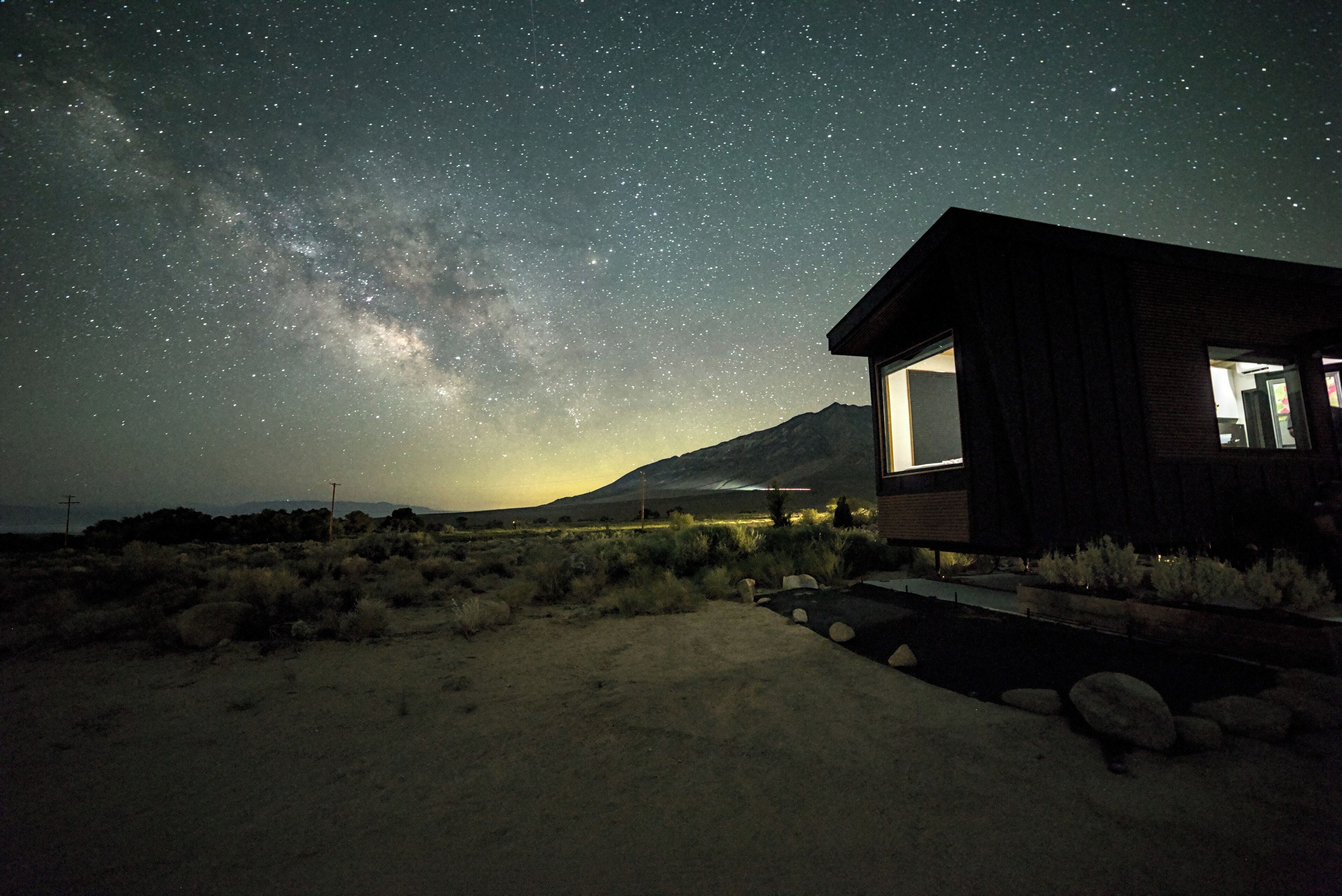 A modern house with a large window, surrounded by a desert landscape, under a starry night sky.
