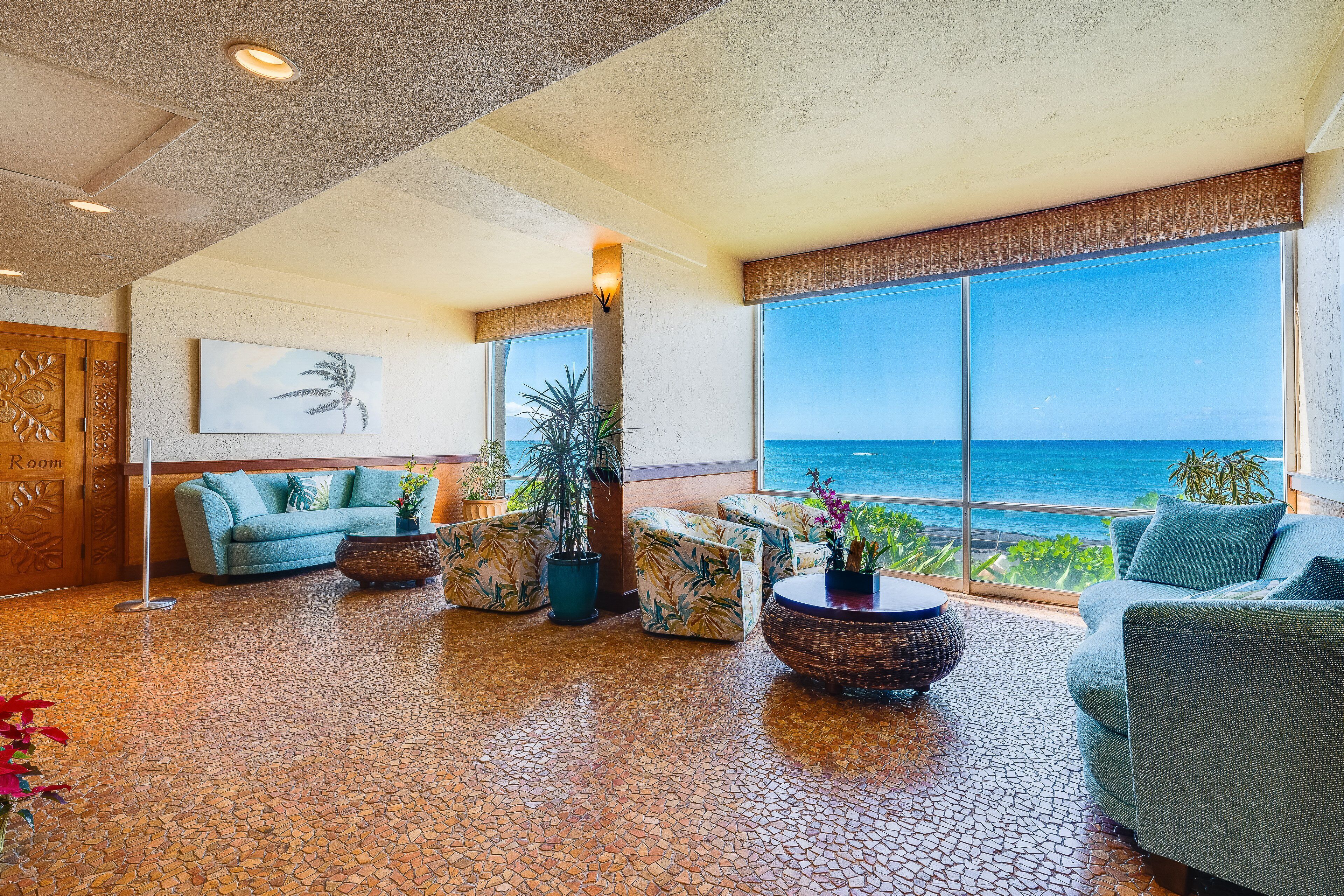 A spacious lobby with a large window offering a view of the ocean, a blue sofa, and tropical-themed decor.