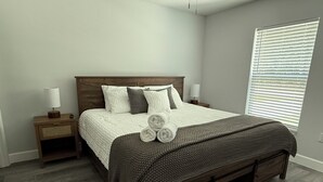 Ein Schlafzimmer mit einem hölzernen Bett, zwei Nachttischen, einem Fenster mit Rollläden und einem grauen Boden.