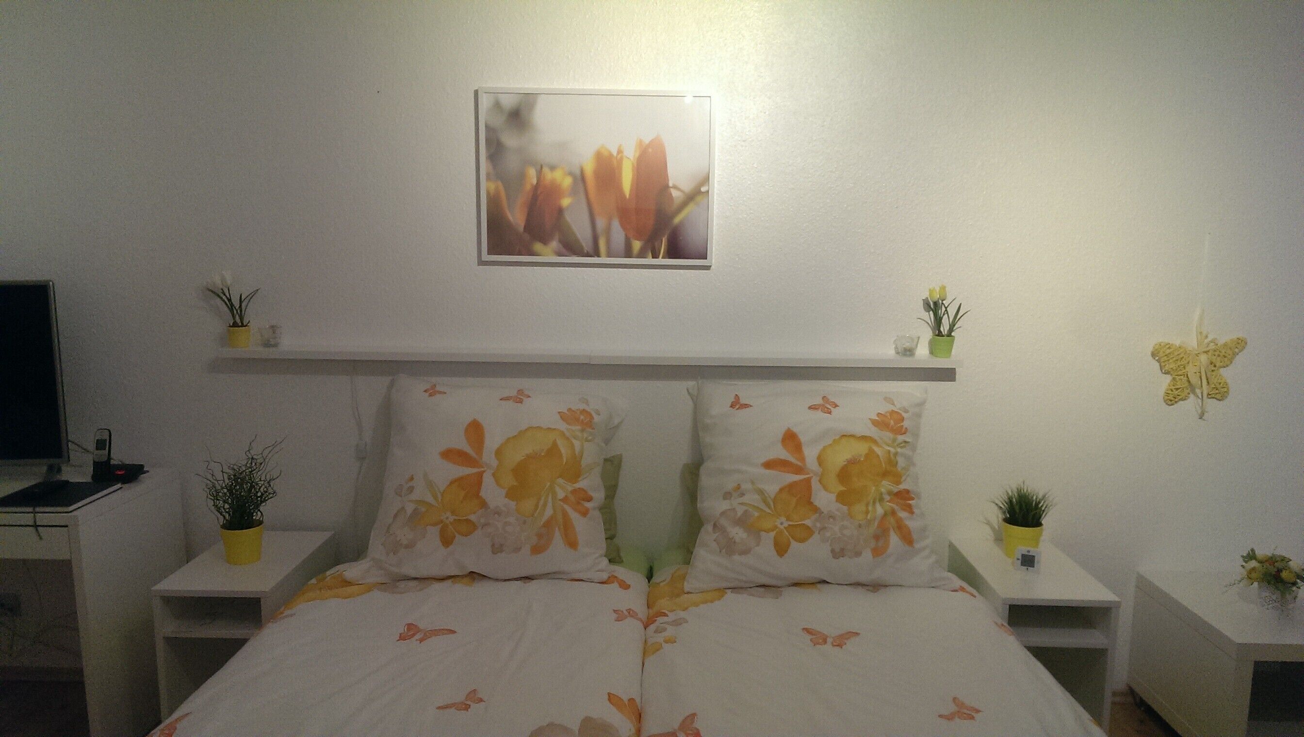Un dormitorio con cama, dos mesitas de noche, televisión e imagen colgada en la pared.