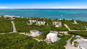An aerial view of a coastal residential area with houses surrounded by dense greenery and a clear view of the ocean. - Villa TreeHaus: Paradise Overlooking Grace Bay (Caicos Islands)