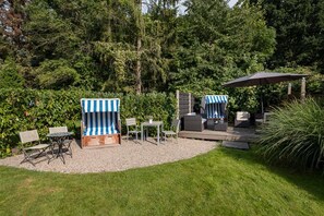 Eine Gartenpatio mit Gartenmöbeln, darunter gestreifte Liegestühle und eine Sitzecke, umgeben von üppigem Grün.