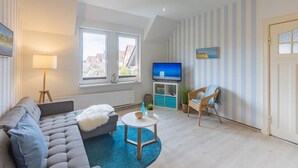 Een woonkamer met een bank, een klein rond tafeltje, een televisie en een stoel.