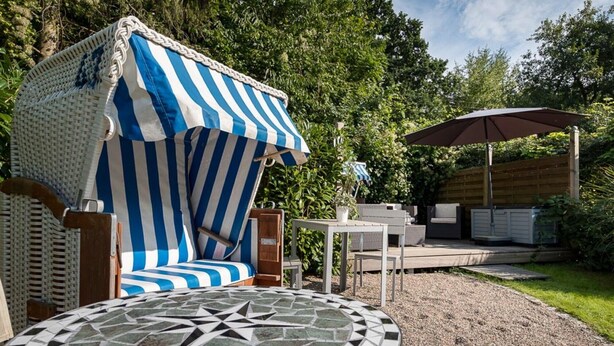 Een terras met een gestreept zonnescherm, tuinmeubels, een mozaiektafel en een jacuzzi.