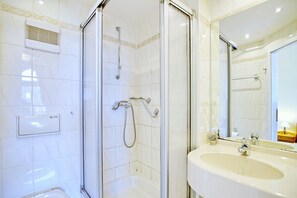 Ein Badezimmer mit einer Duschkabine, einem weißen Waschbecken und einem Spiegel.