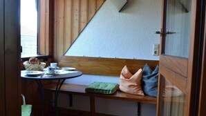 Een kleine kamer met een houten bank, een tafel met een mand brood, en een raam.