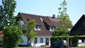 Een twee verdiepingen tellend huis met een schuin dak, een veranda en een oprit waar een auto geparkeerd staat.