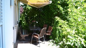 Une terrasse avec une table et des chaises, entourée de verdure.