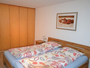 Un dormitorio con una cama doble, un armario de madera, una mesita de noche con una lámpara y un cuadro en la pared.