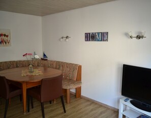 Un comedor con una mesa redonda, sillas, televisor y adornos en la pared.