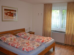 Une chambre à coucher avec un lit en bois, une table de chevet, un radiateur et une fenêtre avec des rideaux.