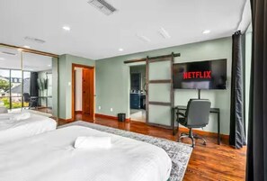 A hotel room with two beds, a desk, a chair, a TV, and a sliding door to the bathroom. - B. Houston Resort Style Pool - EV Charging (Houston)