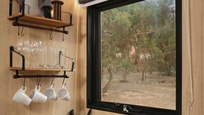 Une cuisine dotée d’un plan de travail en bois, d’un évier en acier inoxydable, d’une fenêtre donnant sur les arbres et d’une étagère où sont rangées des tasses et des verres.