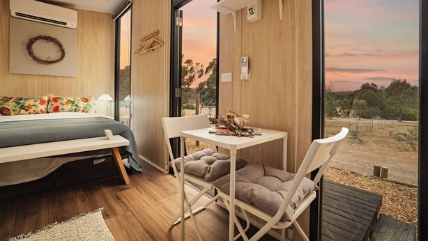 Une chambre moderne avec un lit, une petite table et une chaise, une grande fenêtre donnant sur l’extérieur et un climatiseur fixé au mur.
