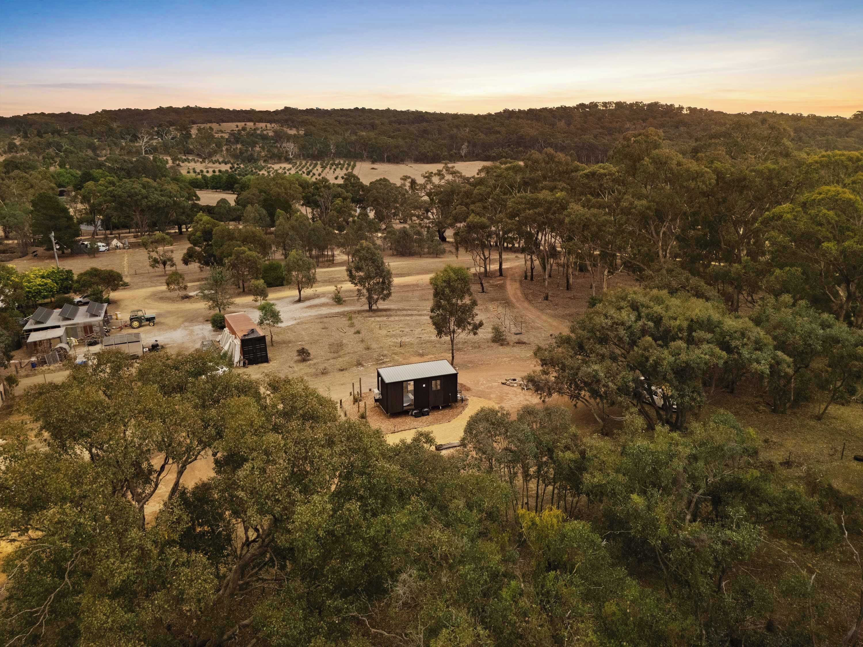 Vue aérienne d’une propriété rurale avec une petite cabane, de vastes champs et quelques arbres dispersés.