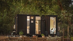 Une petite cabane en bois sombre, à l’intérieur visible, comprenant un coin repas et un lit.