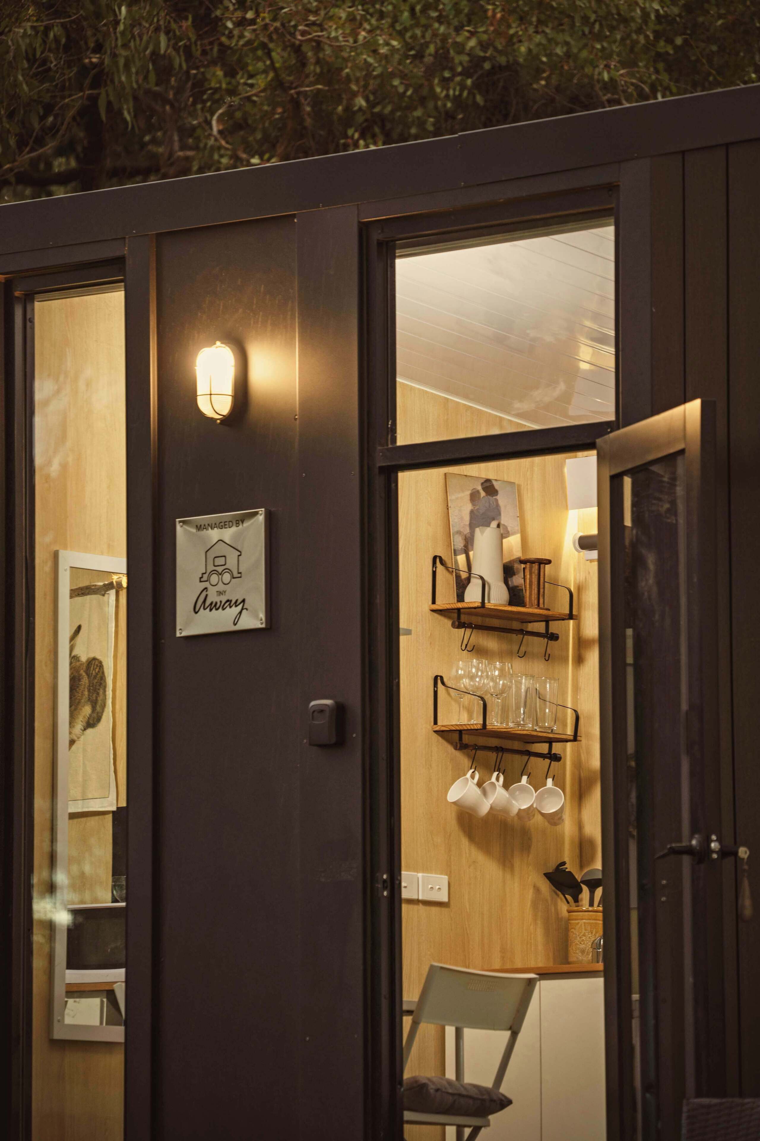 Um interior moderno com parede de madeira, uma placa indicando 'Managed by the Away' e uma estante com xícaras e um vaso.