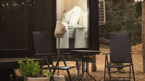 Une petite cabane en bois sombre, dont l’intérieur est visible et comprend un lit, une chaise et une table.