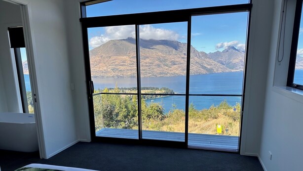 A bedroom with a large sliding glass door leading to a balcony with a scenic view of a lake and mountains. - 1Queenstown - Stunning Lake and Mountain Views (Queenstown)