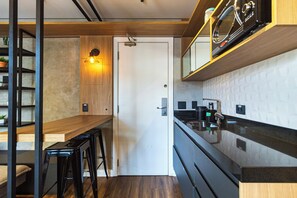 Una cocina moderna con encimera de madera, horno empotrado y microondas. Cuenta con una zona de bar con taburetes y una lámpara fijada a la pared.