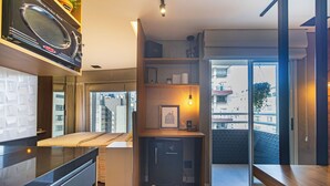Cozinha compacta com micro-ondas, pequena geladeira e área de refeições com banco.