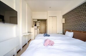Et hotelværelse med en stor seng, et fjernsyn hængt på væggen, et skrivebord og et badeværelse, der kan ses gennem en åben dør.