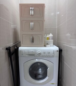 Een praktische, moderne wasruimte met een voorlader wasmachine, een kast met twee lades en een klein plankje met schoonmaakmiddelen.